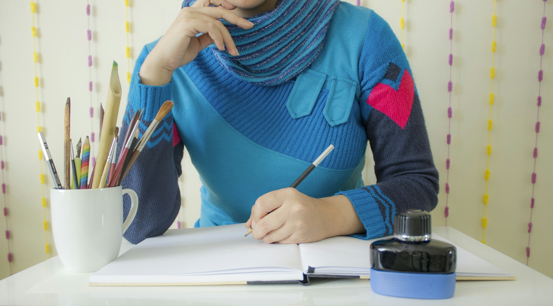 A writer developing an idea in a notebook beside pencils and ink.