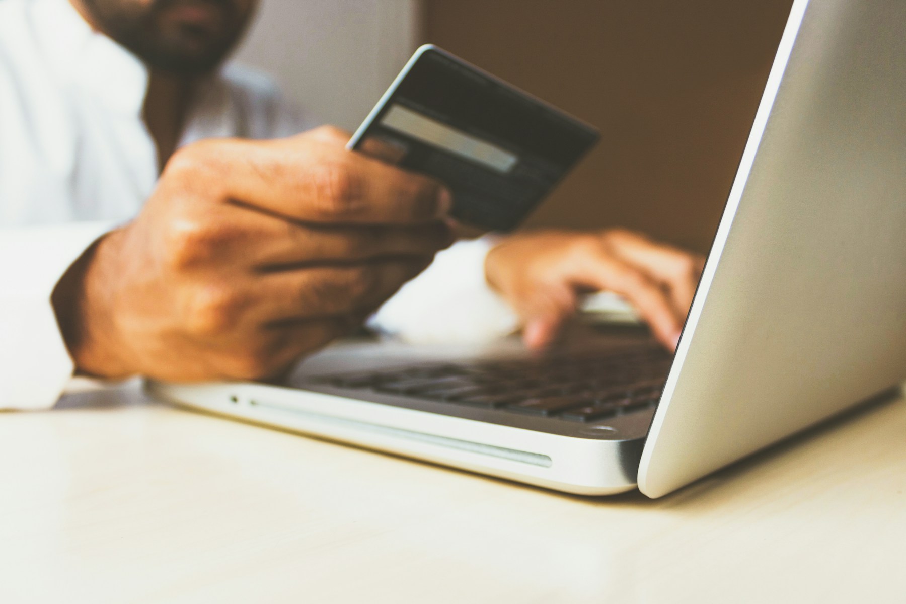 A customer holds a payment card beside a laptop while making an online payment.